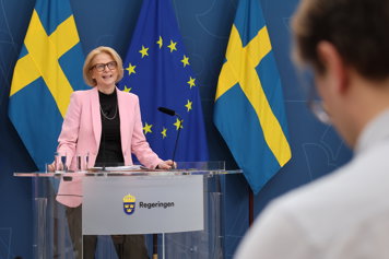 Finansministern talar till journalister vid en pressbriefing. I bakgrunden syns Sverige- och EU-flaggor.