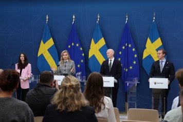 Fyra ministrarna står vid talarstolar framför svenska och eu-flaggor och talar till journalister.