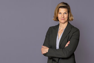 Jämställdhetsminister Nina Larsson står framför en grå vägg och tittar in i kameran.
