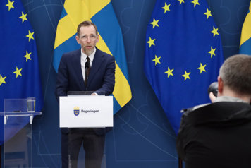 Jakob Forssmed står vid en talarstol, framför svenska och EU-flaggan, i regeringens pressrum.