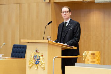 Billström står i talarstolen i riksdagen