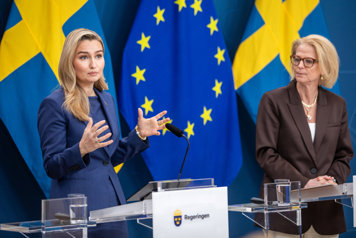 Ebba Busch och Elisabeth Svantesson står vid varsitt podie med flaggor i bakgrunden.