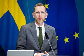 En man talar bakom en talarstol. Svenska flaggan och EU-flaggan bakom honom.