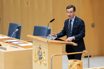 Statsminister Ulf Kristersson står i en talarstol i riksdagens kammare.