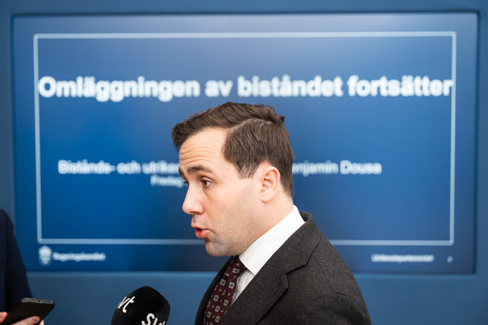 Benjamin Dousa pratar med journalist framför skärm med texten "Omläggningen av biståndet fortsätter".