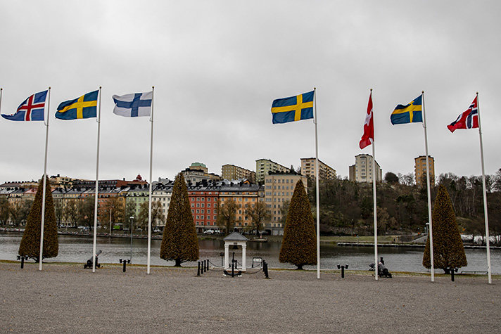 De nordiska flaggorna vajar en gråmulen novembermorgon med vy av Kungsholmen utanför Karlberg slott längs Karlbergssjön. 