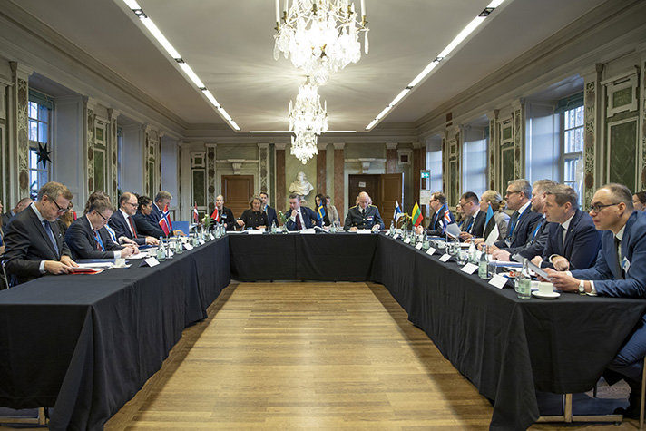 Ministrar och representanter sitter längs ett u-format bord. På borden står flaggorna för de baltiska och nordiska länderna. Centrerat i mitten sitter Pål Jonson. 