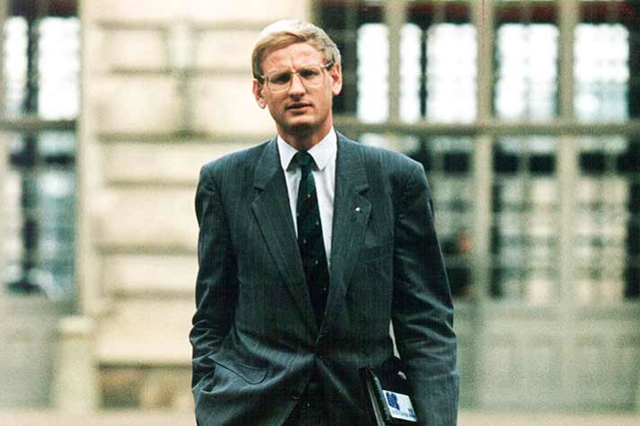 Carl Bildt med en portfölj under armen utomhus framför en byggnad.