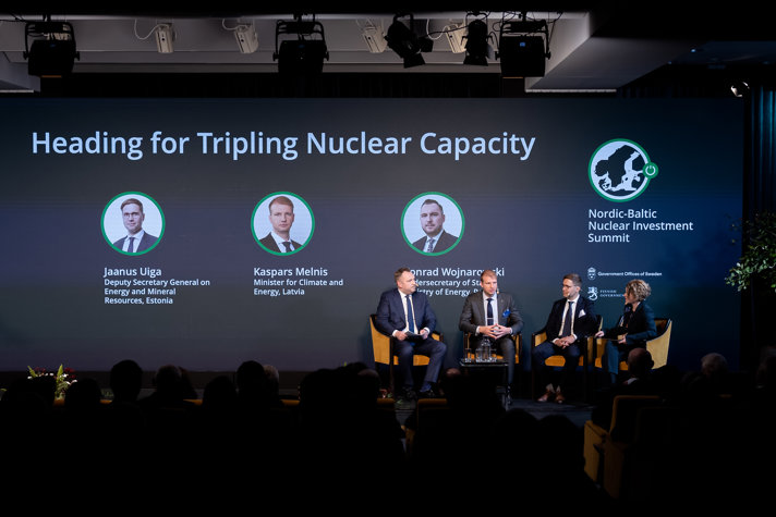 Tre regeringsrepresentanter sitter på scenen i ett samtal som leds av moderatorn Kirsty Hogan