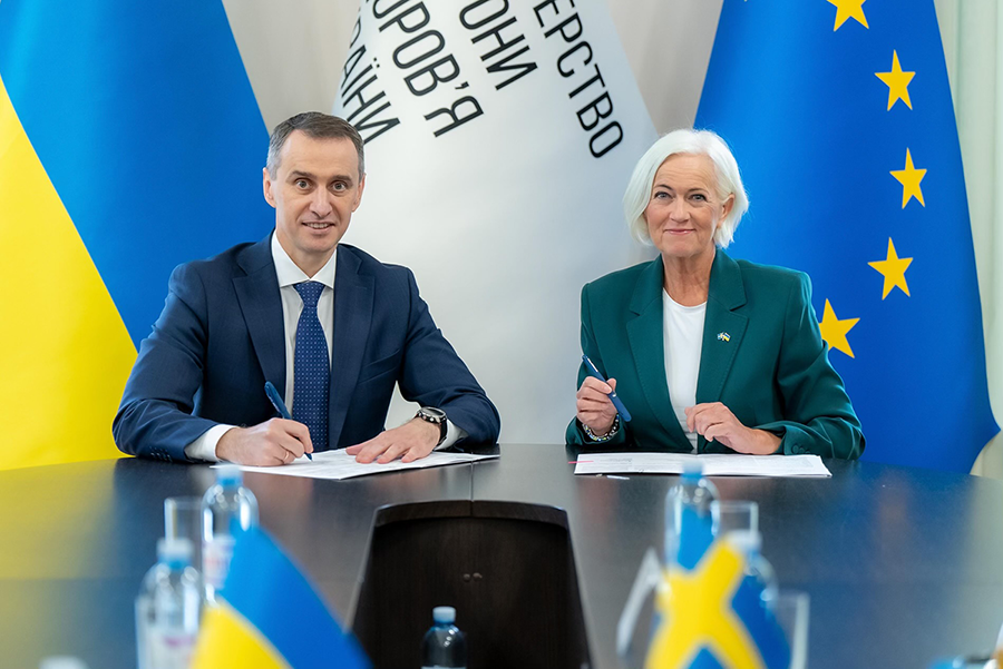 Foto på ministrar som skriver under dokument. Bakom dem står Ukrainas och EU:s flaggor