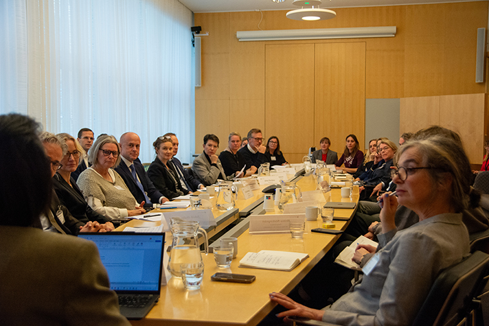 Bild på deltagarna i rundabordssamtalet runt mötesbordet. Alla tittar mot en person som håller anförande.