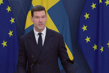 Migrationsminister Johan Forssell vid en talarpulpet med flaggor i fonden.