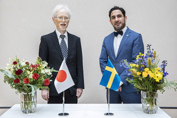 Noke Masaki och Ardalan Shekarabi står bakom ett bord med den japanska och svenska flaggan på.
