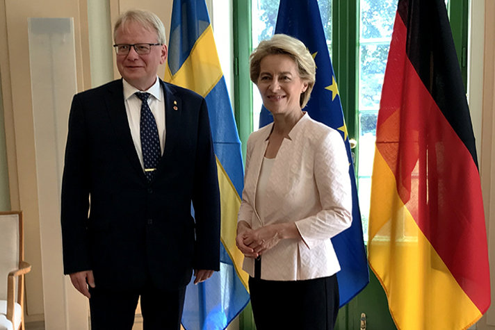 Peter Hultqvist och Ursula von der Leyen i rum mede flaggor i bakgrunden.