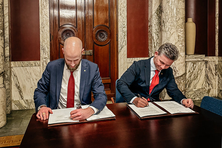 Carl-Oskar Bohlin och Pål Jonson signerar dokument vid ett bord.