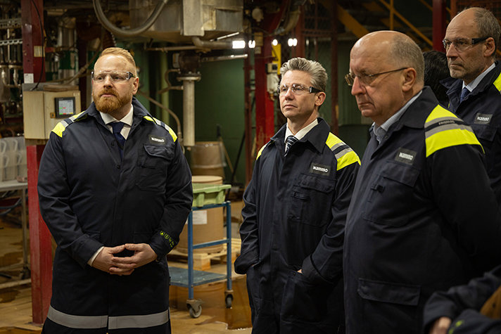 Andreas Burstedt, Pål Jonson och Andrius Kubilius tittar på produktionslinjen inne i Nammos fabrik. De bär alla skyddsrock och skyddsglasögon.