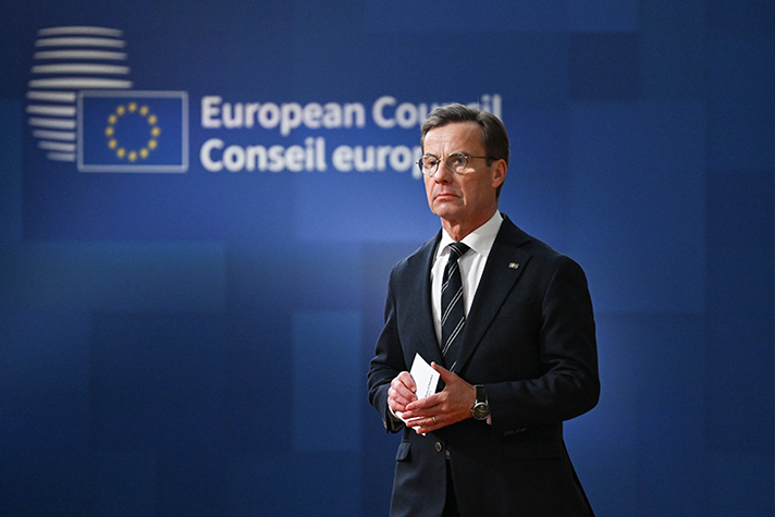 Ulf Kristersson går inomhus framför en blå bakgrund med texten European Council Conseil européen.