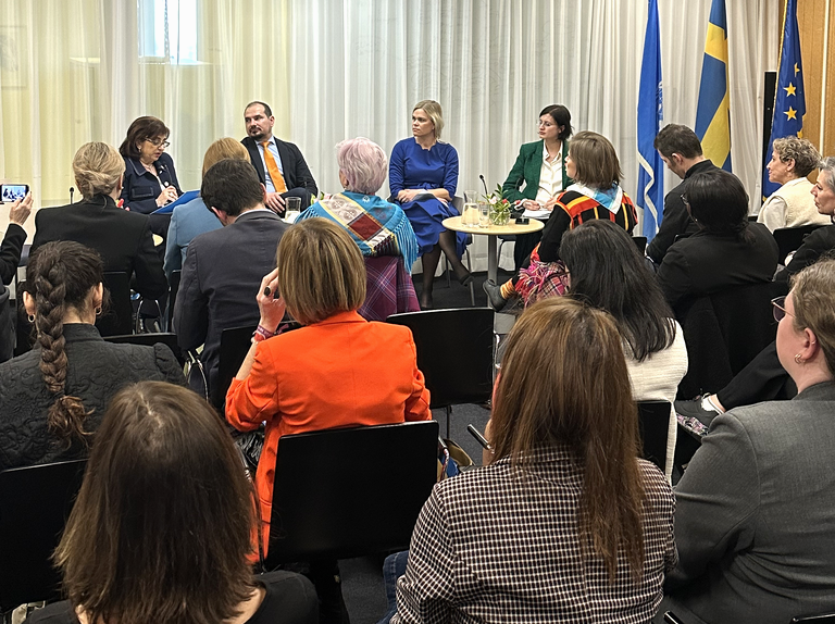 Flera personer sitter tillsammans i ett rum. De flesta sitter och tittar mot några personer som pratar.