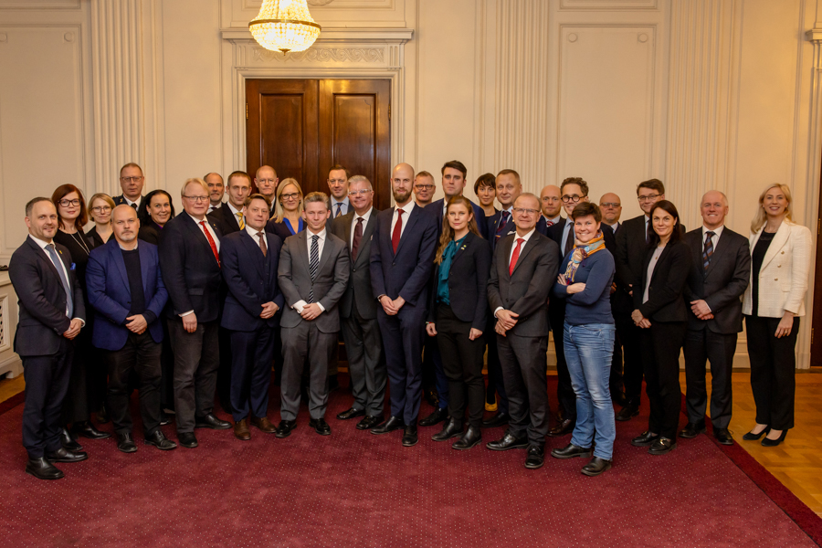 En stor grupp personer uppställda för gruppfoto inomhus.