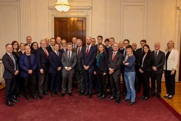 En stor grupp personer uppställda för gruppfoto inomhus.