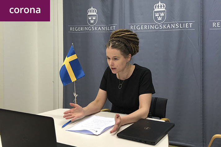 Amanda Lind sitter vid ett bord och tittar mot en skärm.