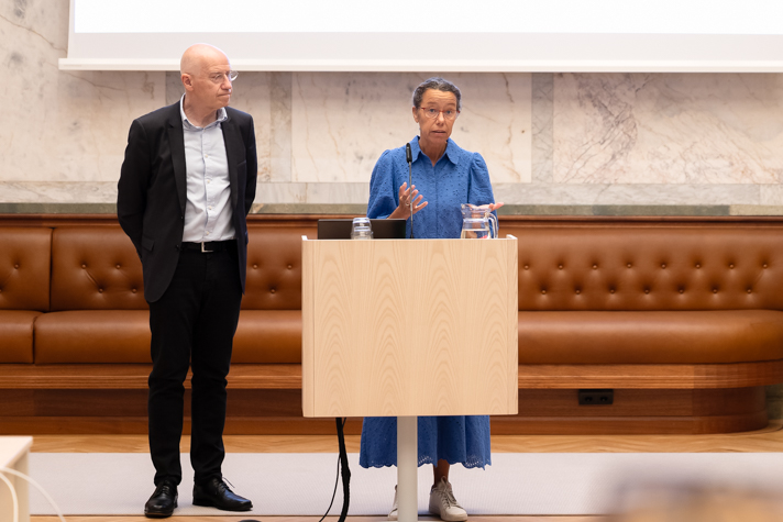Meriam Chatty står vid en talarstol och pratar. Henrik Bachner står vid sidan om.