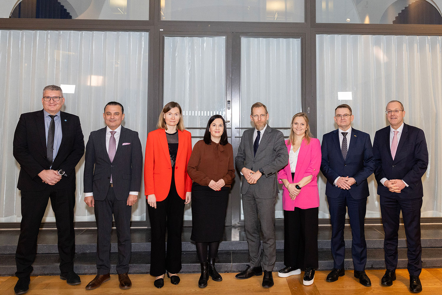 Åtta välklädda personer står framför ett vitt draperi.