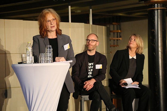 Kulturråd Nina Röhlcke i Berlin står vid talarstolen på scenen och talar till mötesdeltagarna.