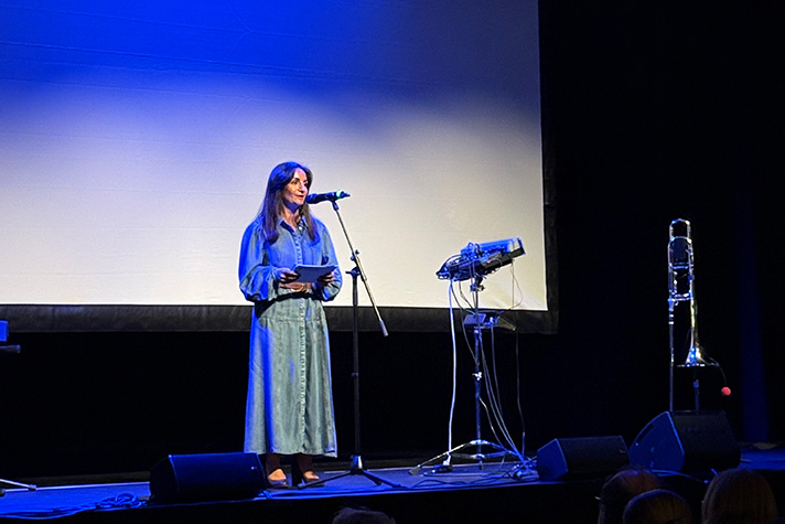 Parisa Liljestrand står på scenen och håller tal. Blå bakgrund bakom henne.