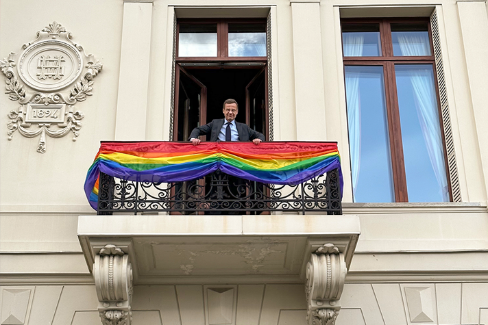 Ulf Kristersson står på en balkong som är prydd med regnbågsflaggan.