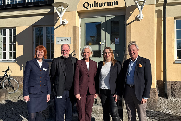 Gruppbild på fyra personer i solsken framför en äldre byggnad.