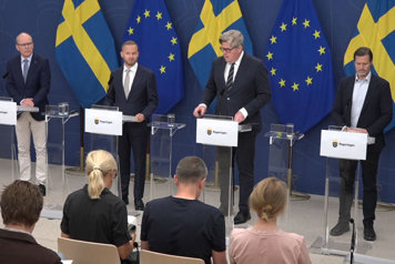 De medverkande står vid var sin talarpulpet framför journalister.
