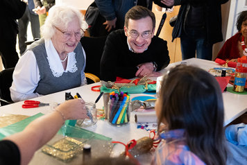 Statsministern sitter med äldre och barn och utför en pysselaktivitet tillsammans.