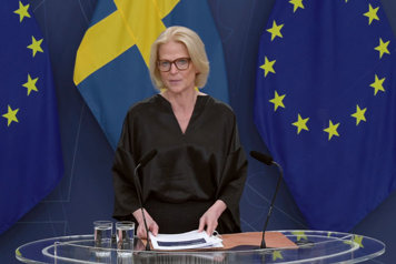 Statsrådet står vid ett ståbord med sveriges och EU:s fana i fonden