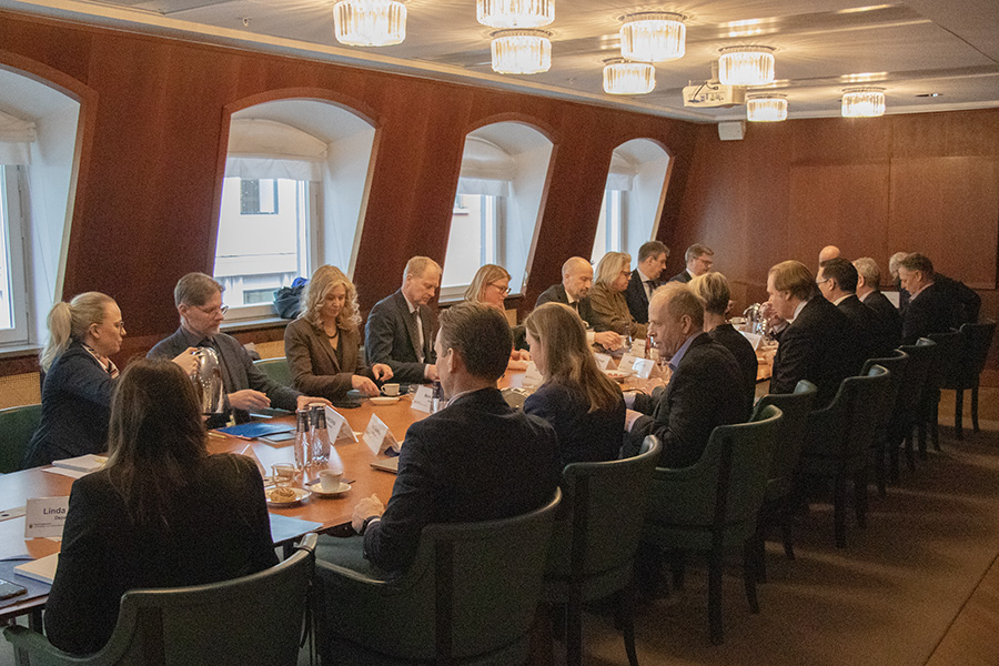 Rådet sitter i salen på sina platser runt ett avlångt bord, ljus kommer in från fönsterna i rummet och lamporna i taket.