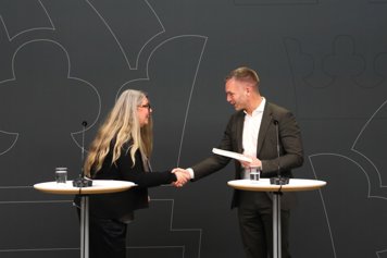 Civilministern tar emot utredningen från den särskilde utredaren, framför en grå bakgrund på pressträffen.