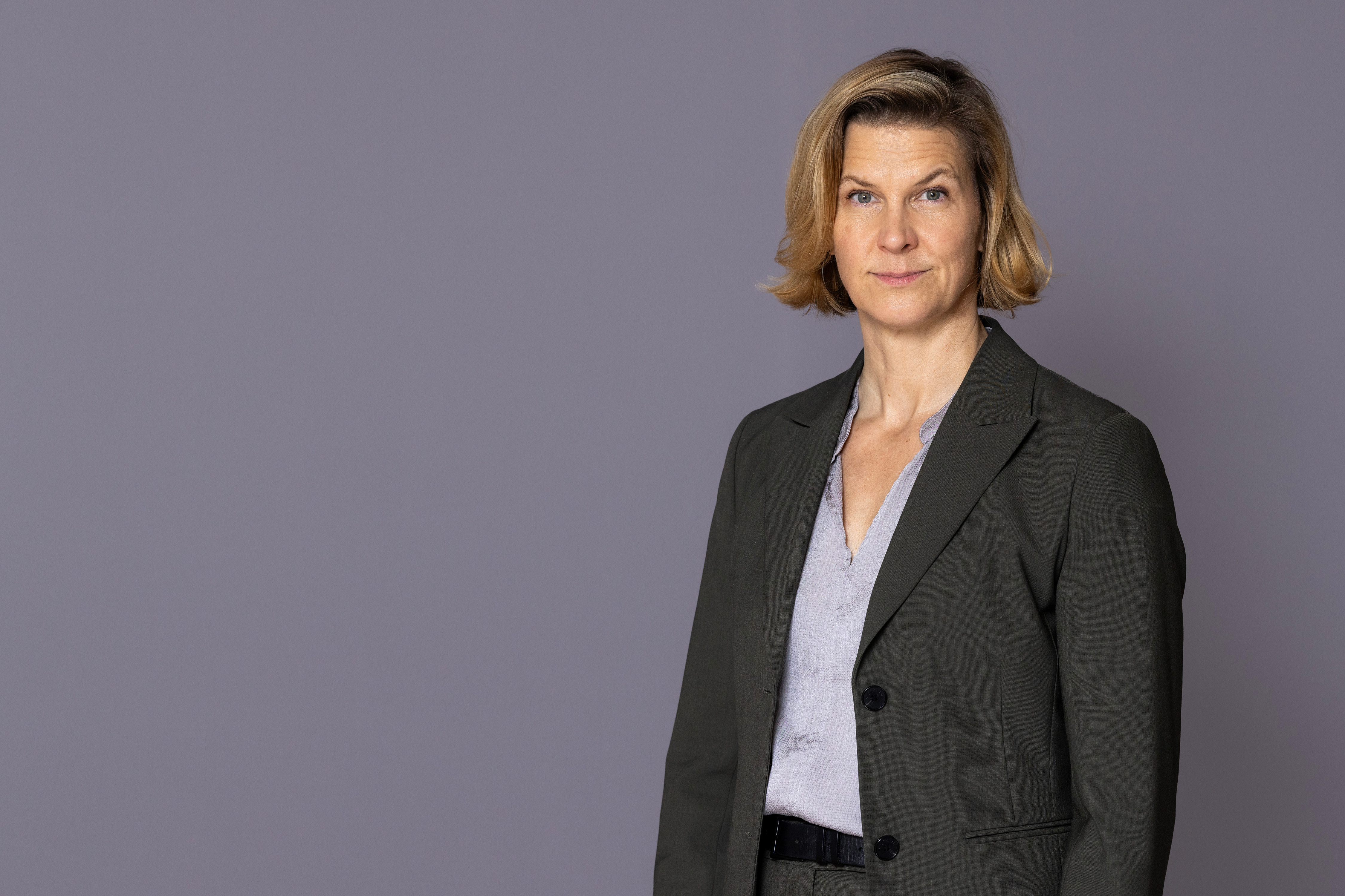 Jämställdhetsminister Nina Larsson står framför en grå vägg och tittar in i kameran.