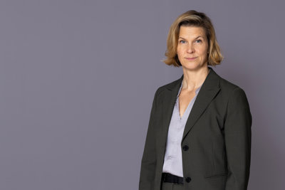 Jämställdhetsminister Nina Larsson står framför en grå vägg och tittar in i kameran.