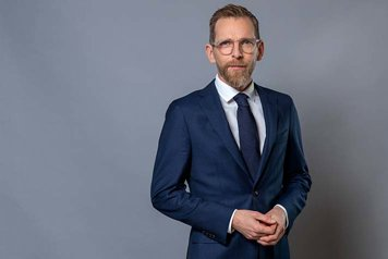 Porträttfotografi på Jakob Forssmed som står framför en grå bakgrund.  