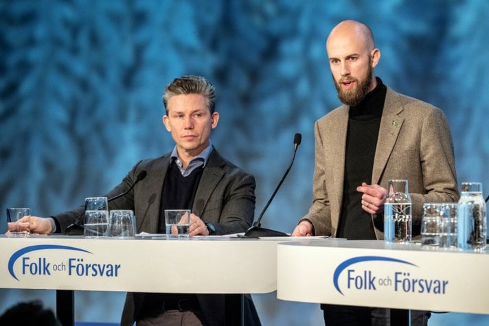 Foto på försvarsminister Pål Jonson och minister för civilt försvar Carl-Oskar Bohlin står  bakom ett bord på en scen.
