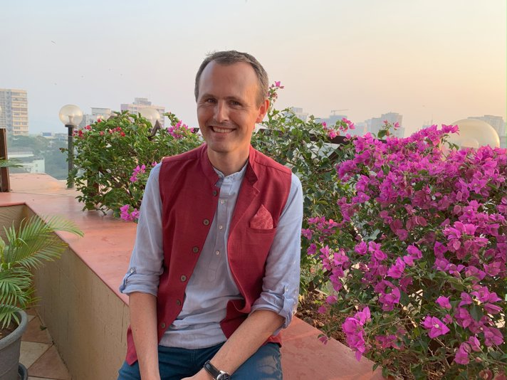 En man ler när han sitter på en takterrass i Indien.