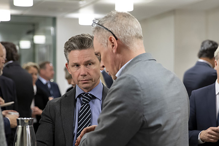 Försvarsminister Pål Jonson står vid ett mingel bland andra personer som man ser ryggen på.