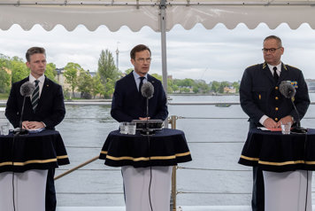 De medverkande står vid var sin talarpulpet på ett båtdäck. I bakgrunden ser man Skeppsholmen.