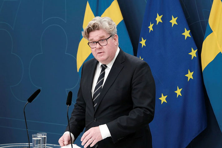 justitieminister Gunnar Strömmer står vid en talarpulpet. Flaggor i fonden.