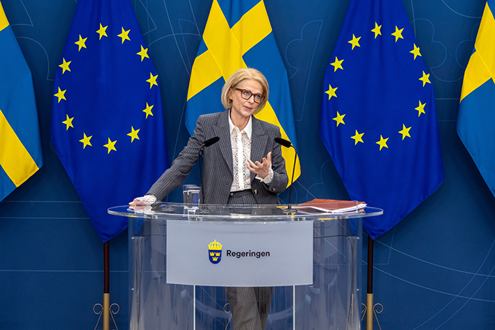 Finansminister Elisabeth Svantesson står vid ett bord på pressträff. I bakgrunden EU-flaggor och svenska flaggor.