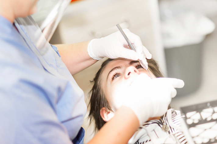 En pojke sitter i tandläkarstolen medan en tandläkare vårdar hans tänder.