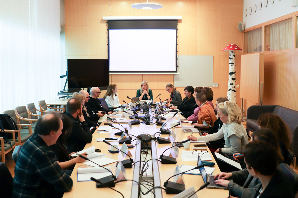 flera personer sitter runt ett sammanträdesbord och pratar.