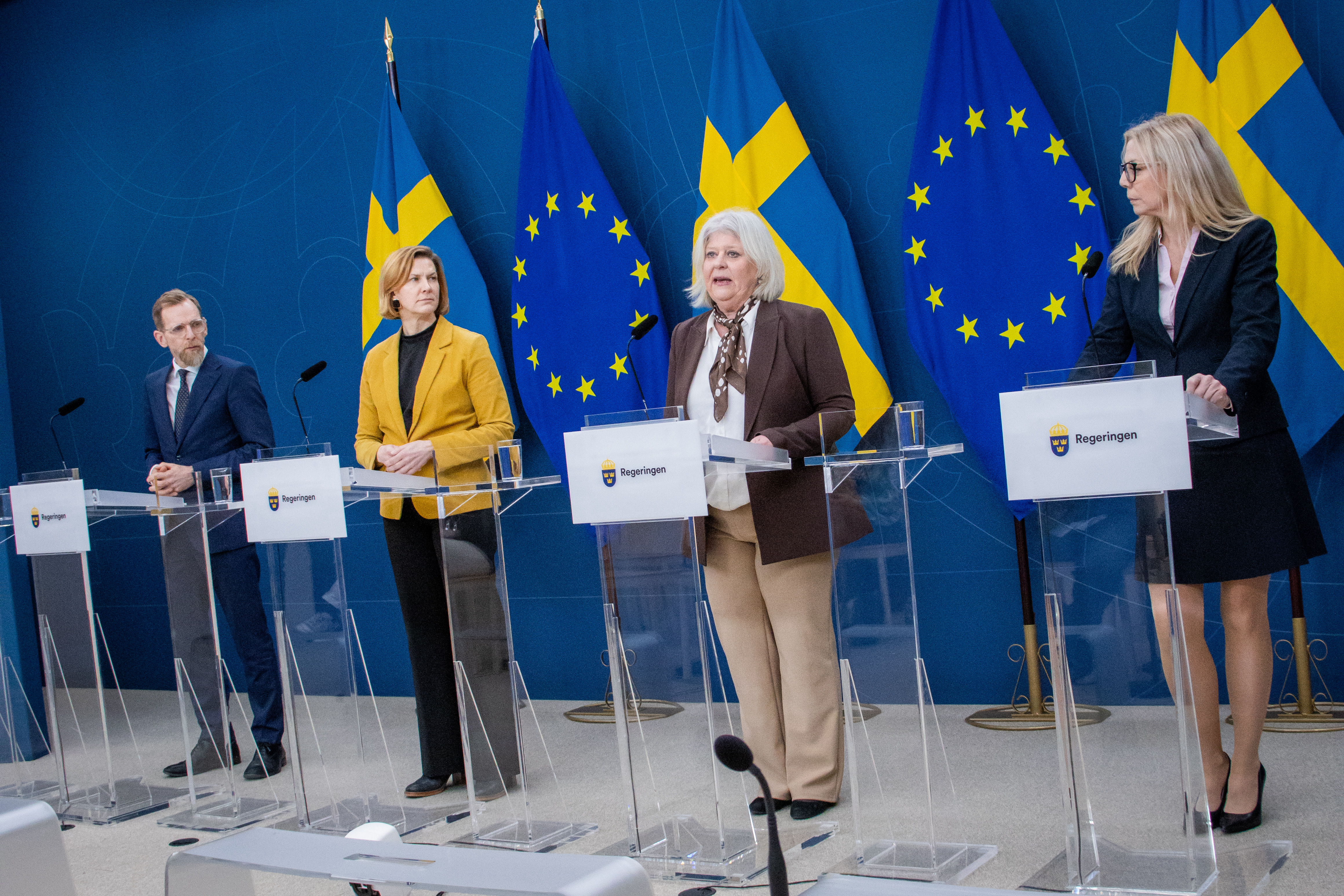 Jakobs Forssmed, Nina Larsson, Camilla Waltersson grönvall och Jessica Stegrud står bakom varsin pelarstol i regeringen pressrum. De står framför svenska flaggor och EU-flaggor.