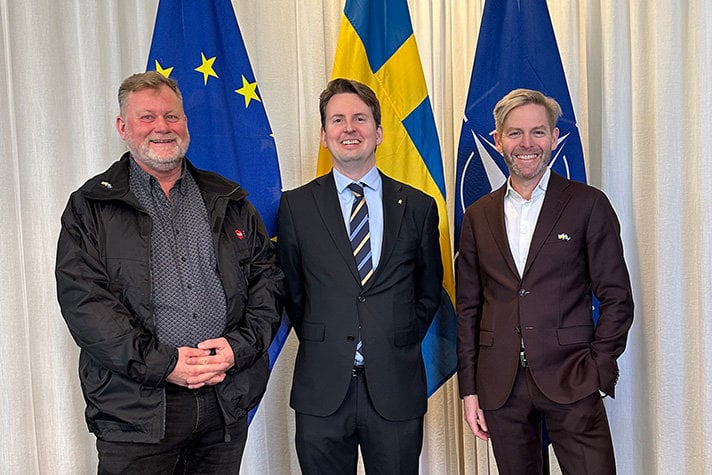 Tre personer står på rad, i bakgrund EU-flaggan, svenska flaggan och Natoflaggan.