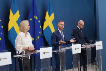 Elisabeth Svantesson, Erik Slottner och Johan Britz står vid podier och talar med journalister.